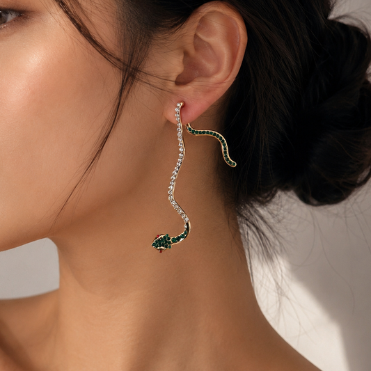 A woman in profile wearing a long, snake-shaped dangle earring with green stone accents and a row of clear stones, photographed against a soft light background.