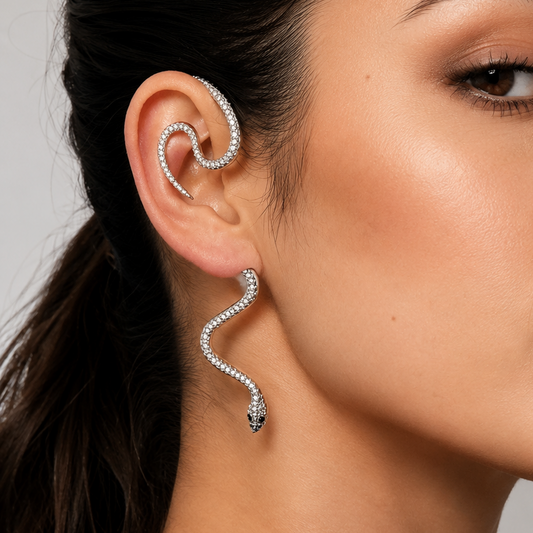 A close-up of a woman's ear wearing a silver-toned, snake-shaped ear cuff and matching snake drop earring, both adorned with small clear stones.