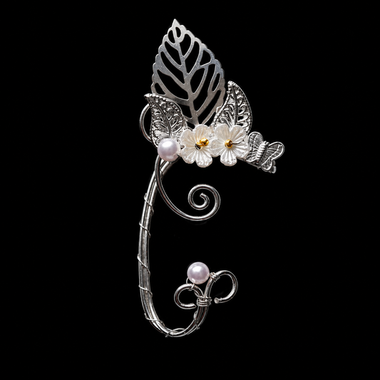 A silver-toned metal hair claw clip styled with a leaf, butterflies, white flowers with yellow centers, and two small pearl-like beads, shown on a solid black background.