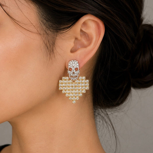 A close-up of a model's ear and neck wearing a dangling skull-shaped earring adorned with clear rhinestones and small red gemstone details.
