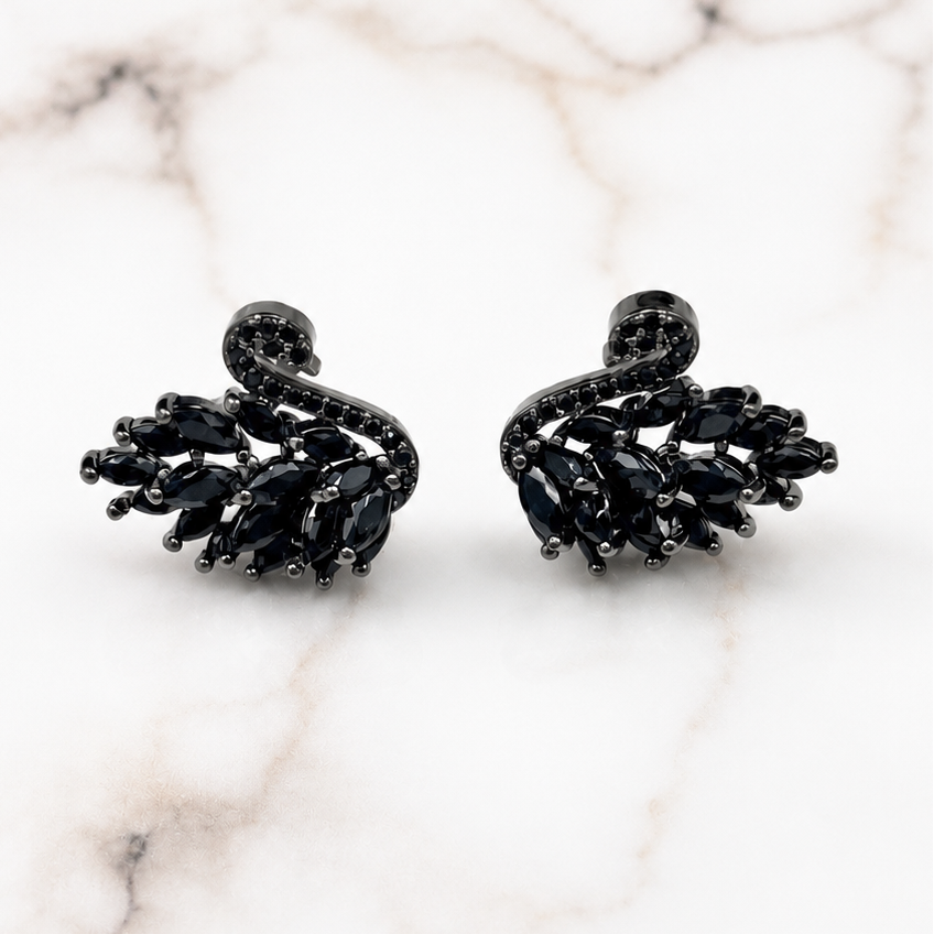 A pair of black crystal swan stud earrings displayed on a white marble surface with gray veining.