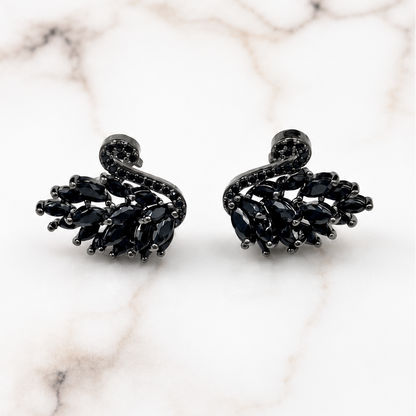 A pair of black crystal swan stud earrings displayed on a white marble surface with gray veining.
