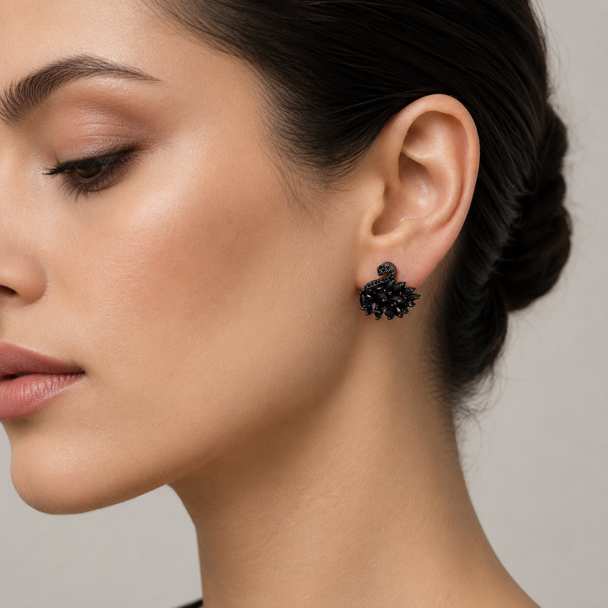 A close-up of a woman's ear wearing a small black floral cluster stud earring against a soft light gray background.