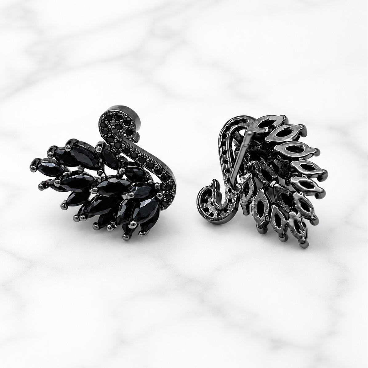 A pair of black metal and black gemstone leaf-shaped earrings displayed on a white marble background.