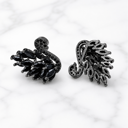A pair of black metal and black gemstone leaf-shaped earrings displayed on a white marble background.