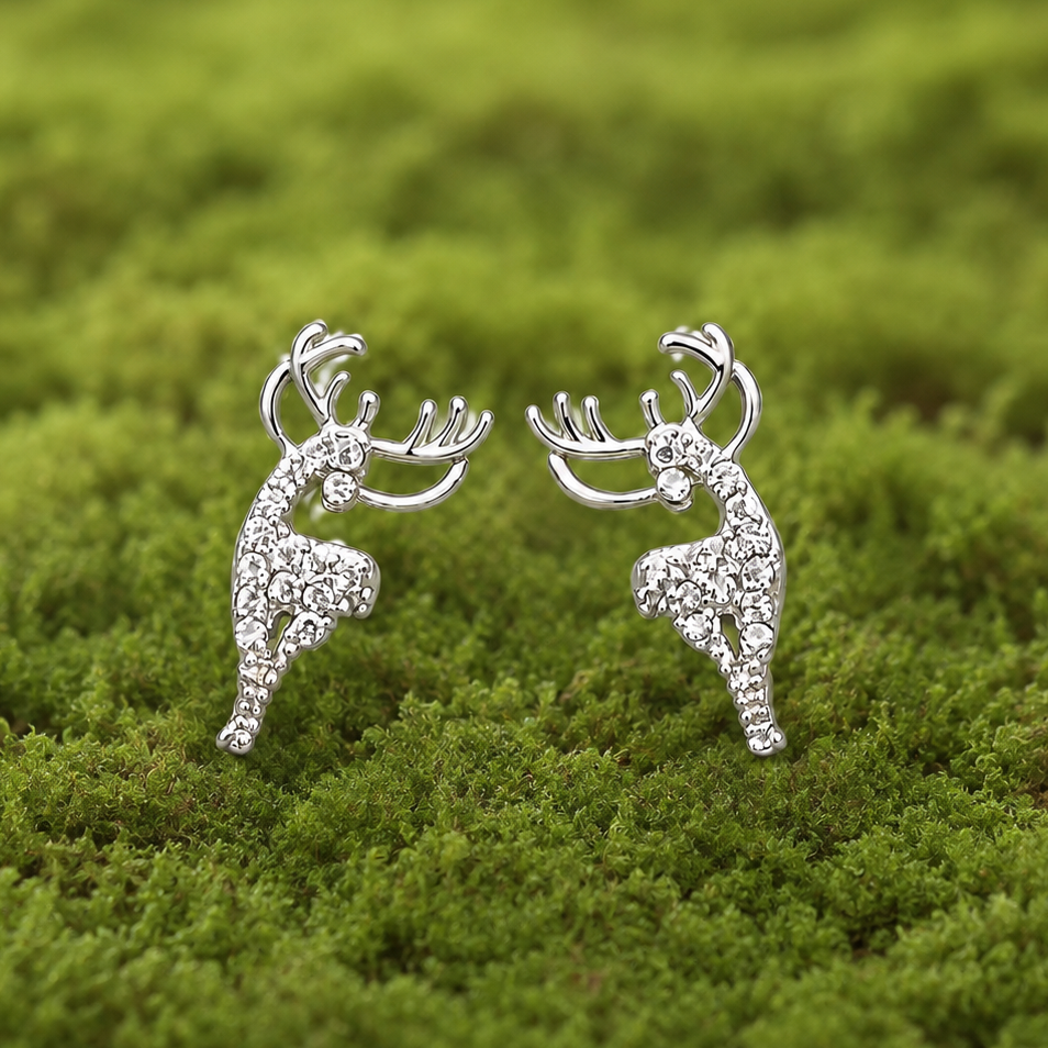 A pair of silver-toned stud earrings shaped like leaping deer, each set with small clear stones, photographed on a soft green moss background.