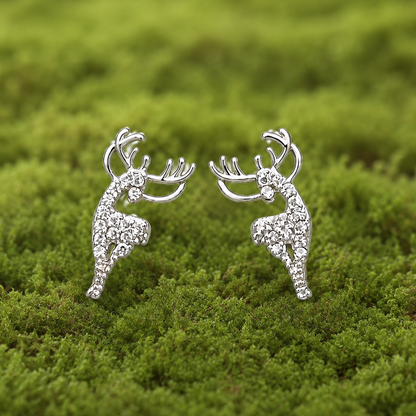 A pair of silver-toned stud earrings shaped like leaping deer, each set with small clear stones, photographed on a soft green moss background.