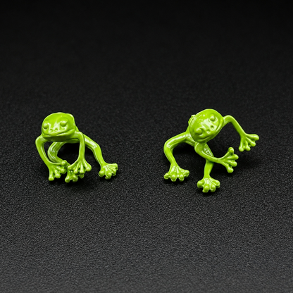 Two bright green frog-shaped stud earrings displayed side by side on a dark textured background.