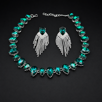 A jewelry set featuring a silver-tone necklace and matching drop earrings with emerald-cut green crystals and silver pavé fringe details, displayed on a dark background.