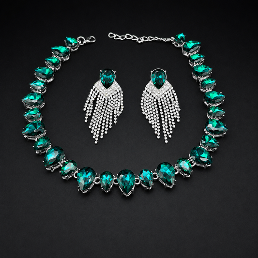 A jewelry set featuring a silver-tone necklace and matching drop earrings with emerald-cut green crystals and silver pavé fringe details, displayed on a dark background.