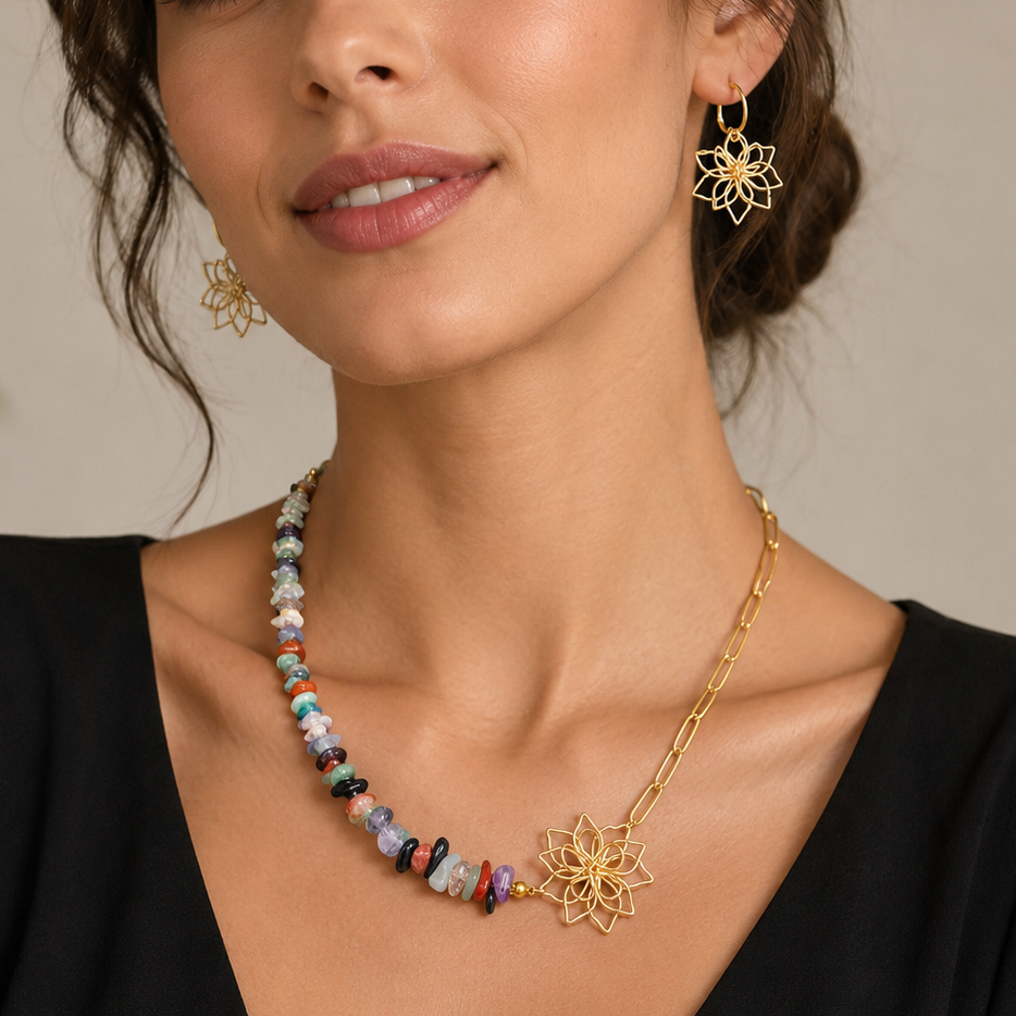A woman wearing a gold necklace with a sunburst pendant and matching gold hoop earrings, styled with a black top against a soft beige background.