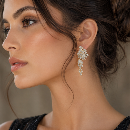 A close-up side profile of a woman wearing a delicate, leaf-shaped dangle earring adorned with sparkling clear stones in a gold-tone setting.