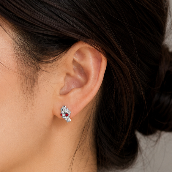 A close-up side profile of a woman with dark hair in a bun, wearing a small silver-toned floral stud earring with clear gemstones against a neutral gray background.