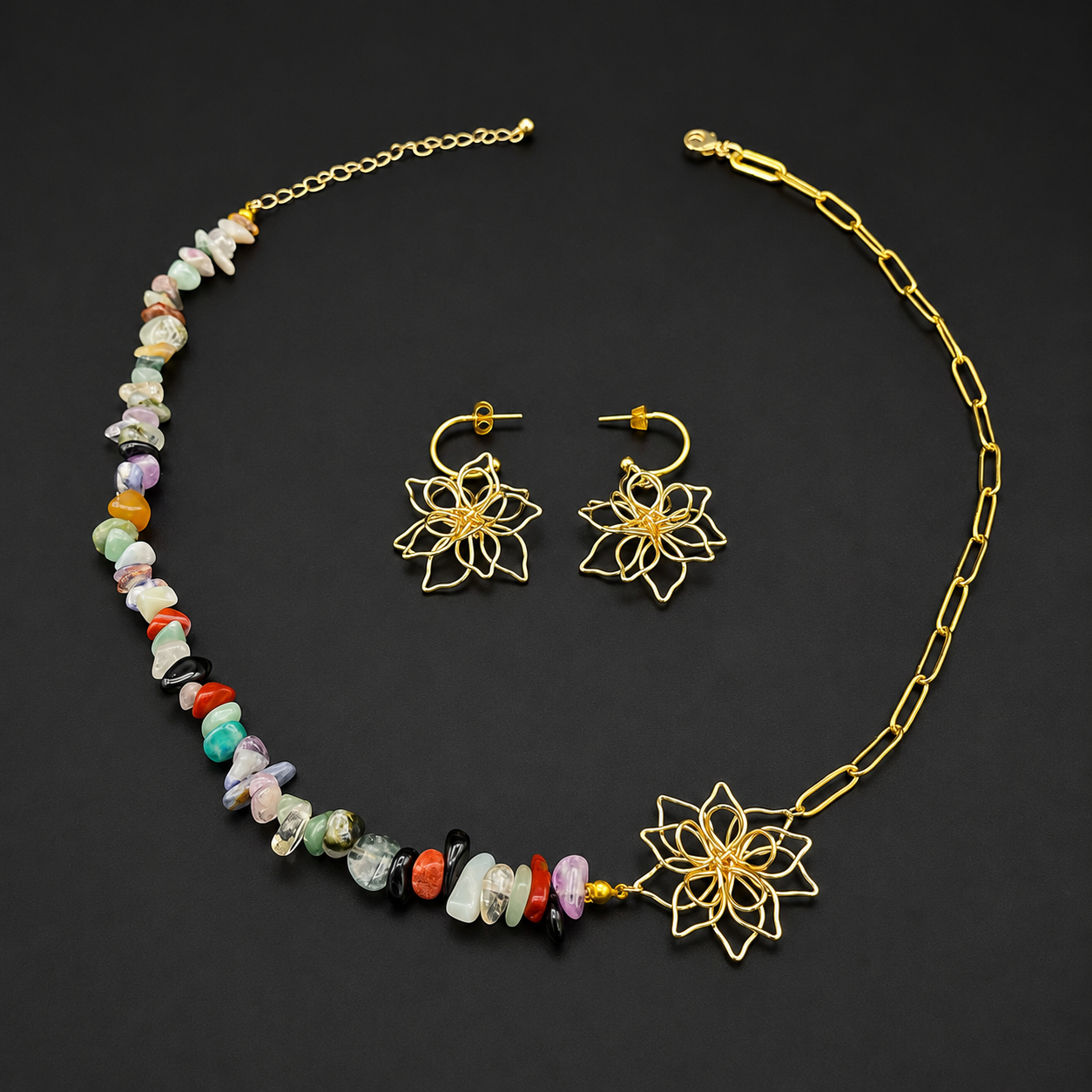 A gold-tone necklace and matching drop earrings set on a black background. The necklace features a beaded strand with multicolored stone chips and a large gold lotus flower at the end, paired with a chain link section and clasp closure.