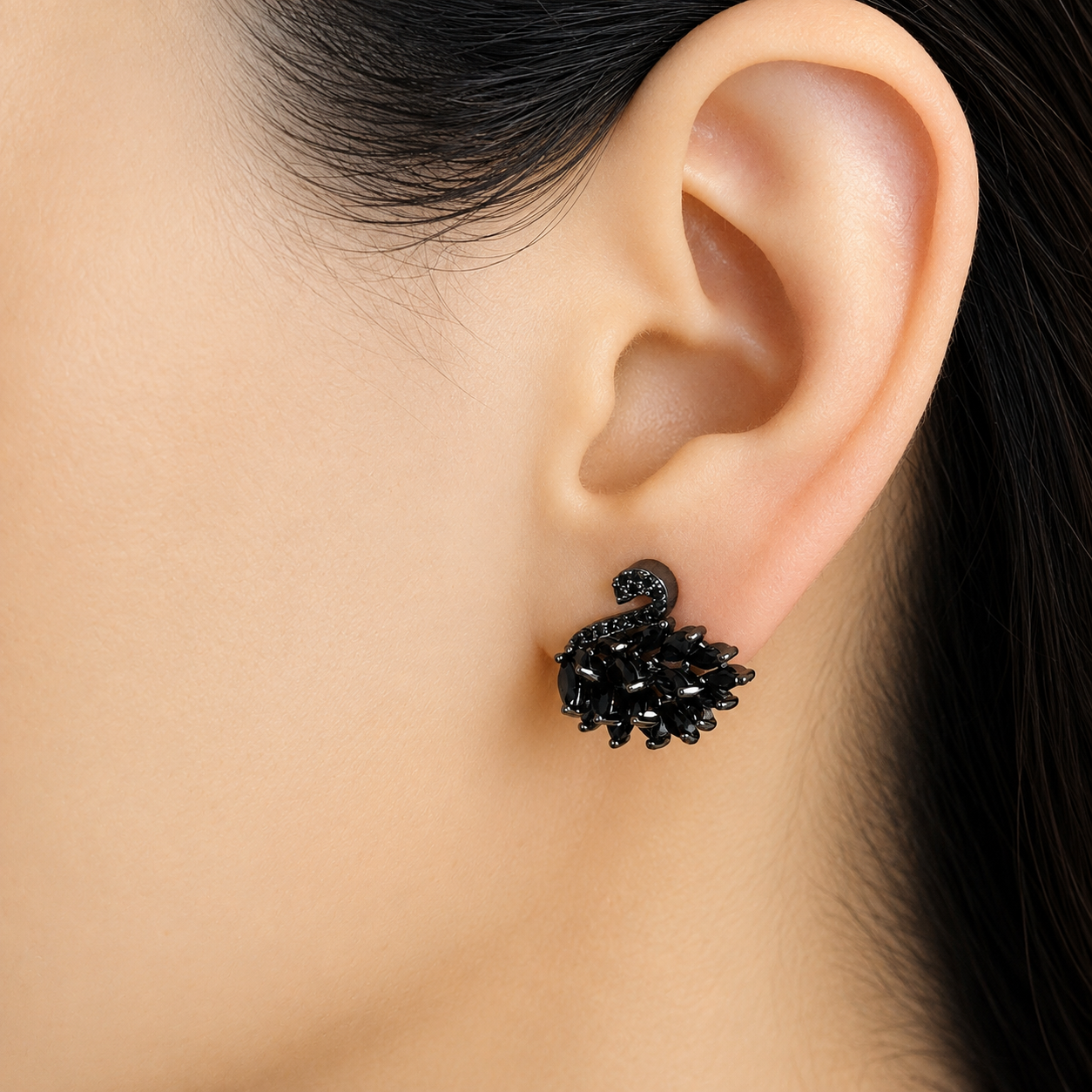 A close-up of a person's ear wearing a black textured stud earring with a curved, snake-like top.