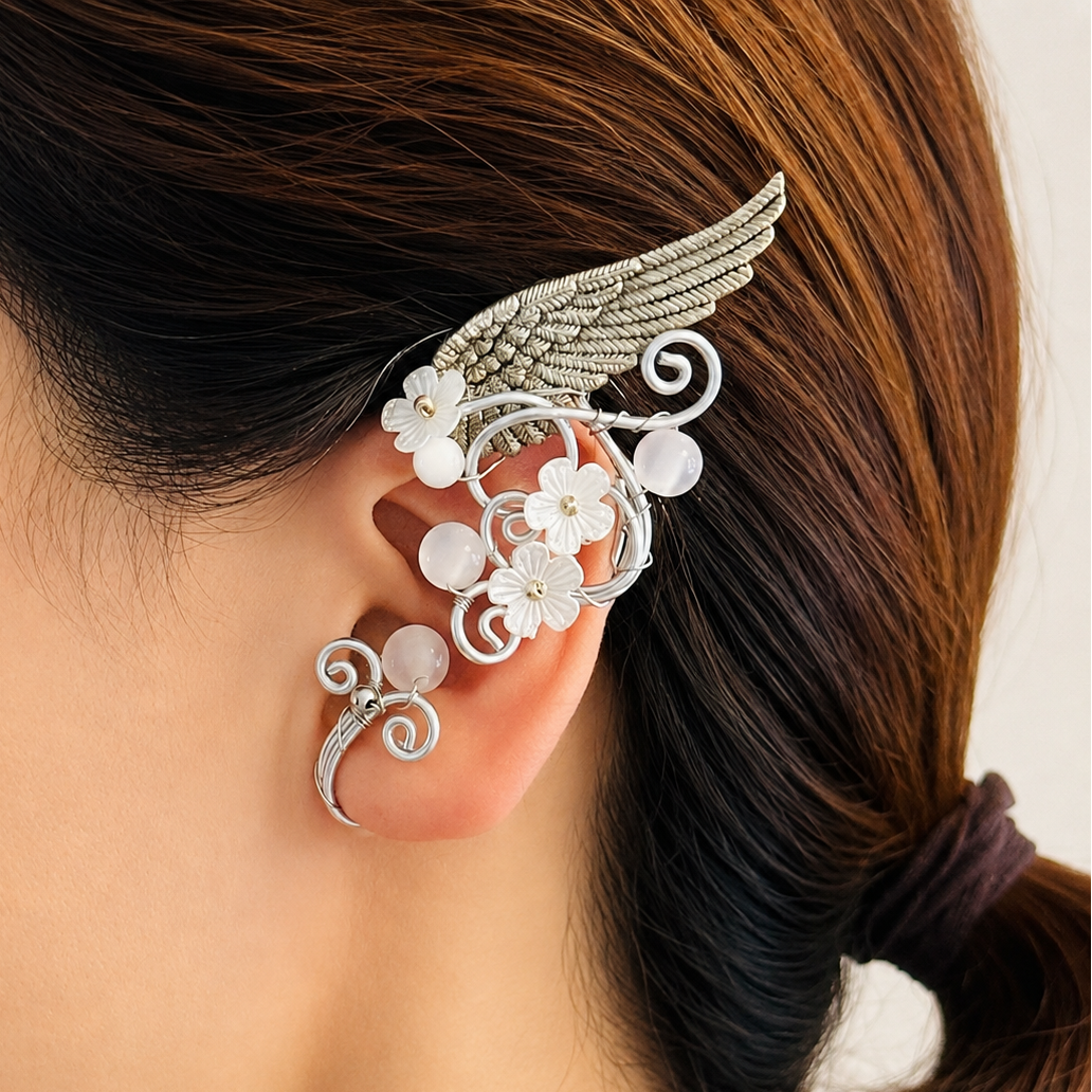 A close-up of a woman's ear wearing a silver wing and white flower ear cuff, with her dark brown hair tied back.
