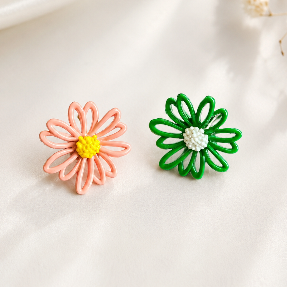 Two small flower-shaped earrings on a soft white surface. One earring is peach-pink with a yellow center, and the other is green with a white center.
