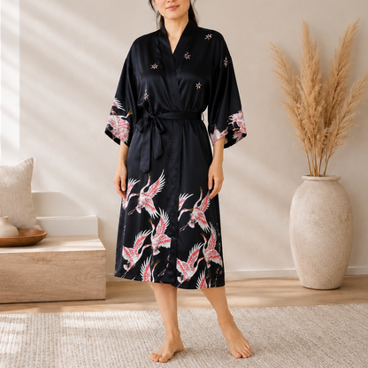 a black kimono-style robe with pink and white crane prints and small floral embroidery. The robe has wide sleeves and a self-tie waist.