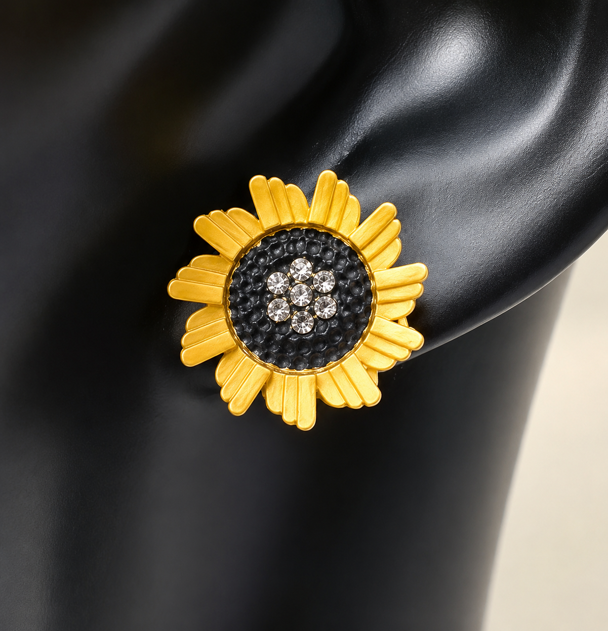 A yellow and black sunflower-shaped brooch with a crystal-encrusted center, displayed on a black mannequin bust.