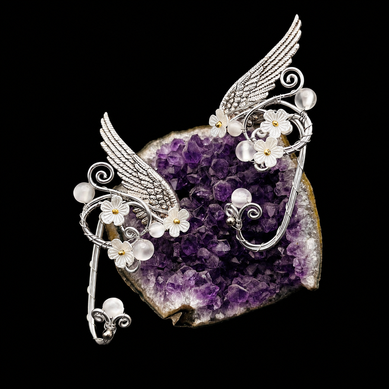 Silver-toned winged brooch with white pearl-like beads and small white flowers, displayed on top of a purple amethyst geode slice against a black background.