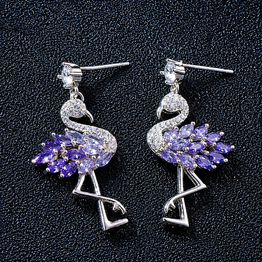 A pair of silver-tone flamingo dangle earrings with purple marquise-cut stones, displayed on a textured black background.