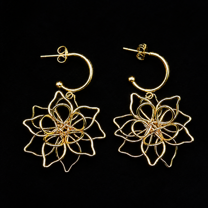 A pair of gold hoop earrings with intricate, layered wire floral dangle charms, displayed against a solid black background.