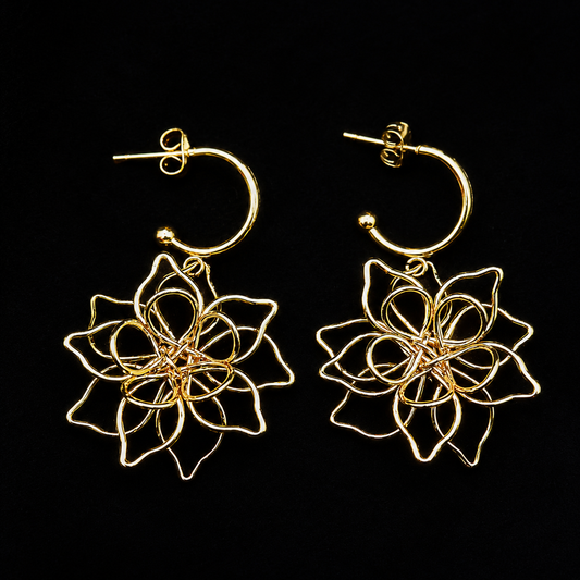 A pair of gold hoop earrings with intricate, layered wire floral dangle charms, displayed against a solid black background.