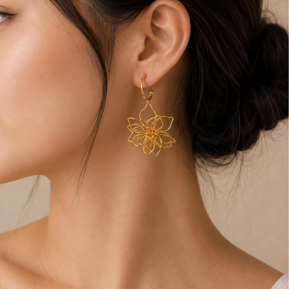 A close-up side profile of a woman wearing a delicate gold wire flower dangle earring, set against a soft beige background.