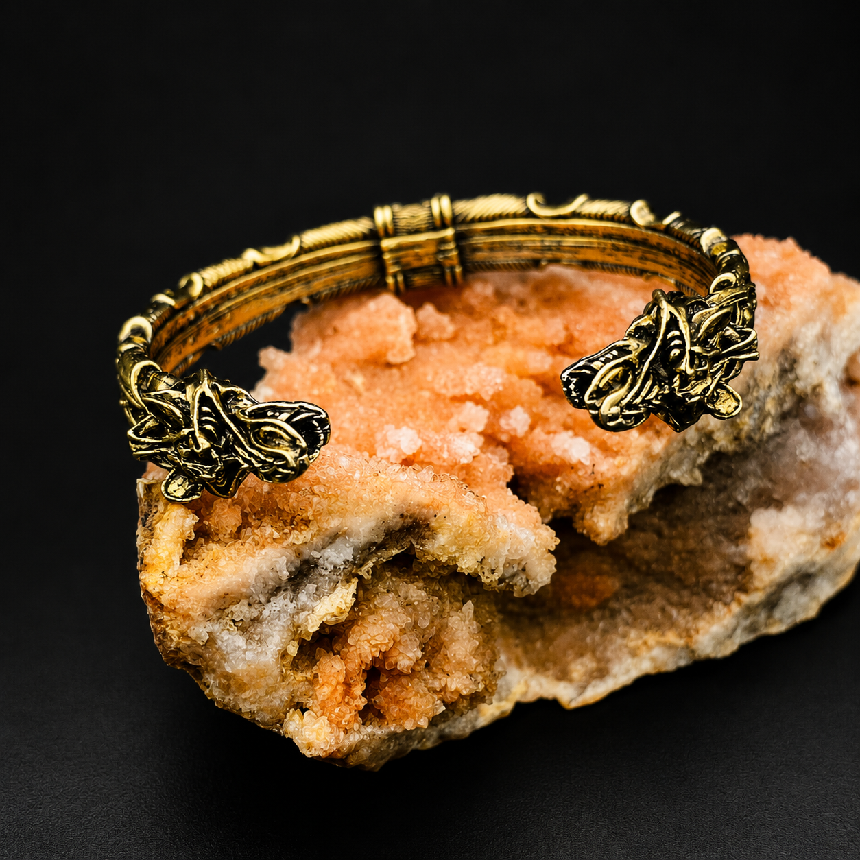 An ornate antique gold-toned metal cuff bracelet displayed on a rough orange and beige mineral specimen against a black background.