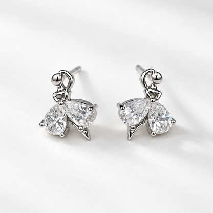 A pair of silver-toned butterfly stud earrings with clear teardrop-cut gemstones, displayed on a clean, light gray textured fabric background.