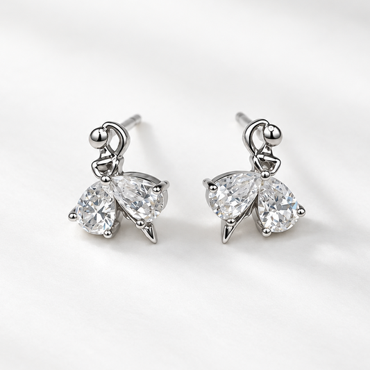 A pair of silver-toned butterfly stud earrings with clear teardrop-cut gemstones, displayed on a clean, light gray textured fabric background.