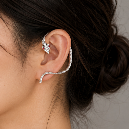 A woman in profile wearing a delicate silver ear cuff with a small floral cluster on the earlobe and a curved wire extending toward the temple, against a soft gray background.