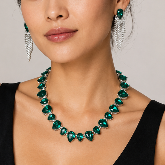 A woman wearing a green gemstone necklace and matching drop earrings with silver chain details, photographed against a plain light gray background.