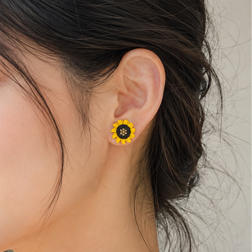 A close-up of a woman wearing a small yellow flower stud earring with a black center, shown against a soft light background.