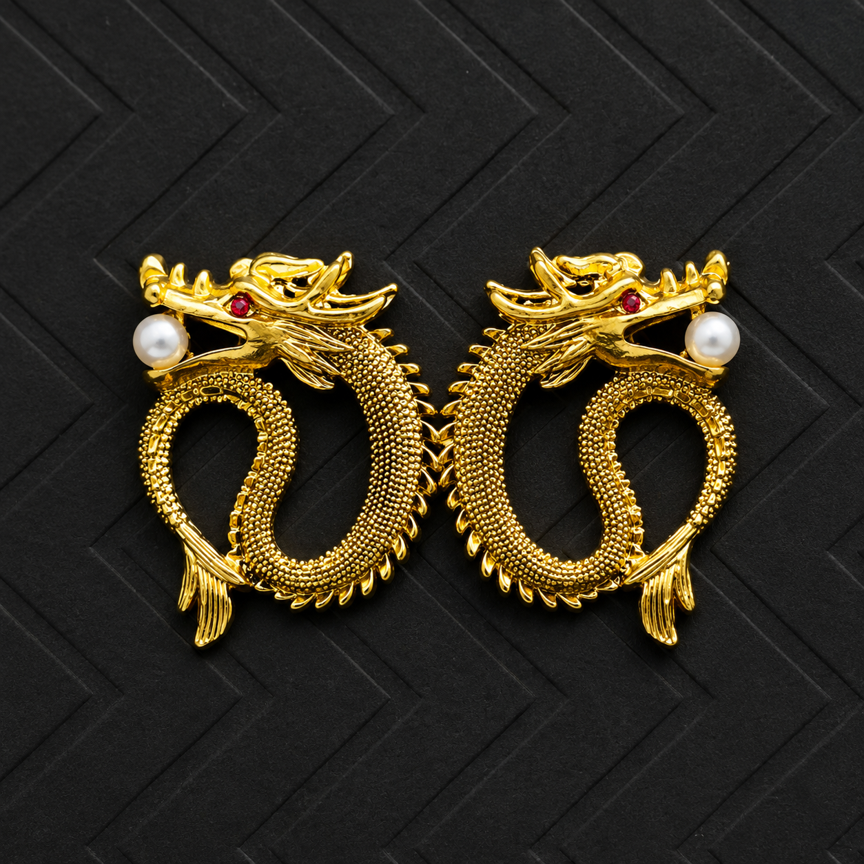 A pair of gold dragon-shaped earrings with white pearl accents and small red gemstone eyes, displayed on a black textured background.