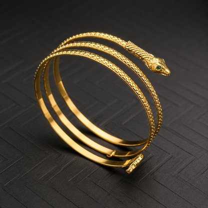 A gold snake-head cuff bracelet with textured and smooth bands, featuring a small green eye detail on the snake head, displayed on a dark textured background.