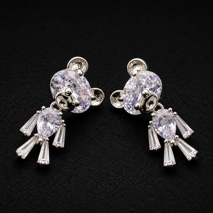 A pair of silver-tone dangle earrings featuring large oval clear crystals on the top and teardrop-shaped clear crystals dangling below, displayed on a textured black background.