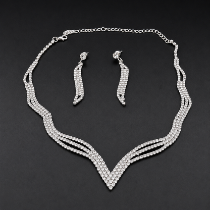 A silver-tone jewelry set featuring a multi-strand V-shaped necklace and matching drop earrings, both adorned with clear rhinestones, displayed on a dark background.