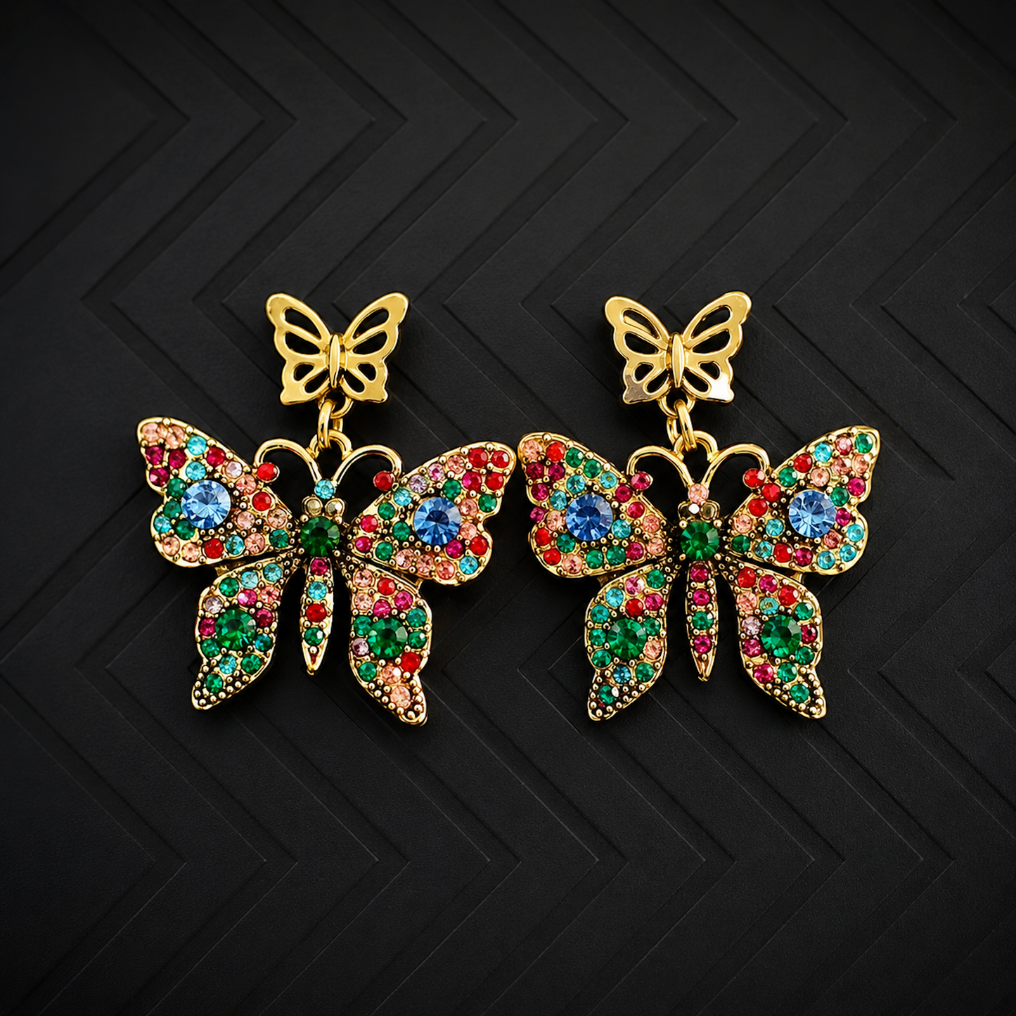A pair of gold butterfly drop earrings embellished with multicolored rhinestones in red, green, and blue