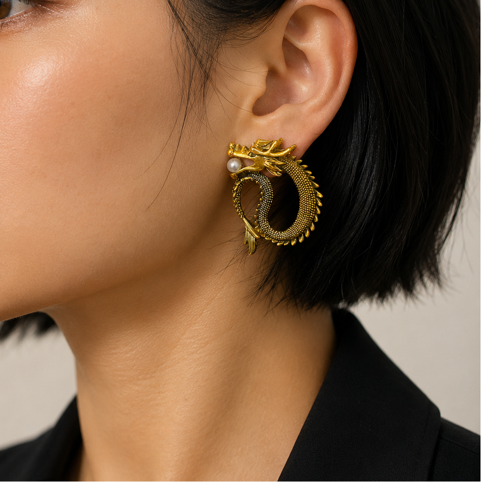 A close-up of a woman with short black hair wearing a large gold dragon-shaped hoop earring with small pearl accents, paired with a black collared top against a light beige background.