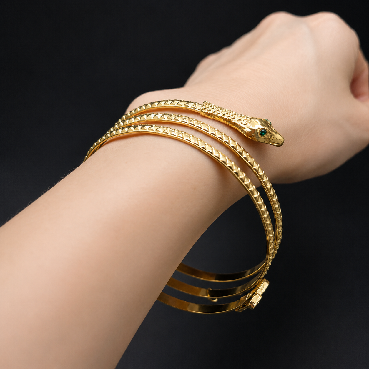 A close-up of a person's wrist wearing a gold snake-themed bangle bracelet with a detailed snake head and textured bands, set against a solid black background.