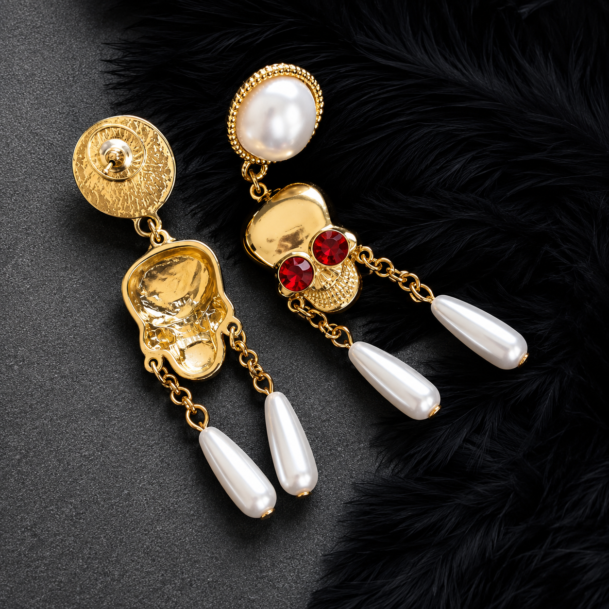 A pair of ornate gold-tone dangle earrings with white pearl-like drops, red gemstone accents, and textured gold details, displayed on a dark textured surface with black feather trim.
