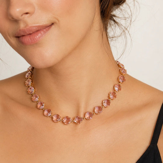 A close-up of a woman wearing a delicate necklace with round blush pink gemstones in a rose gold setting.