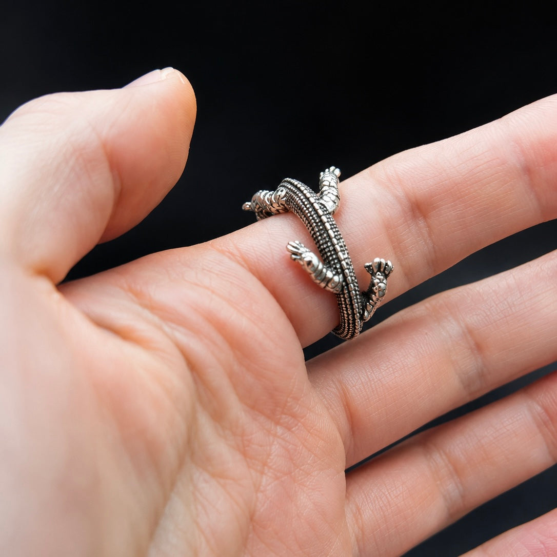 A silver-toned textured ring shaped like a coiled snake or worm, shown worn on a person's finger against a dark background.