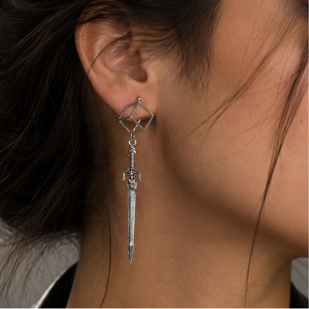 A close-up side profile of a woman with dark hair in a bun wearing a long silver dangle earring with a geometric top and a sword-shaped drop.
