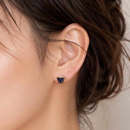 Close-up of a woman wearing a small triangular stud earring with a dark blue faceted stone in a gold-tone setting.